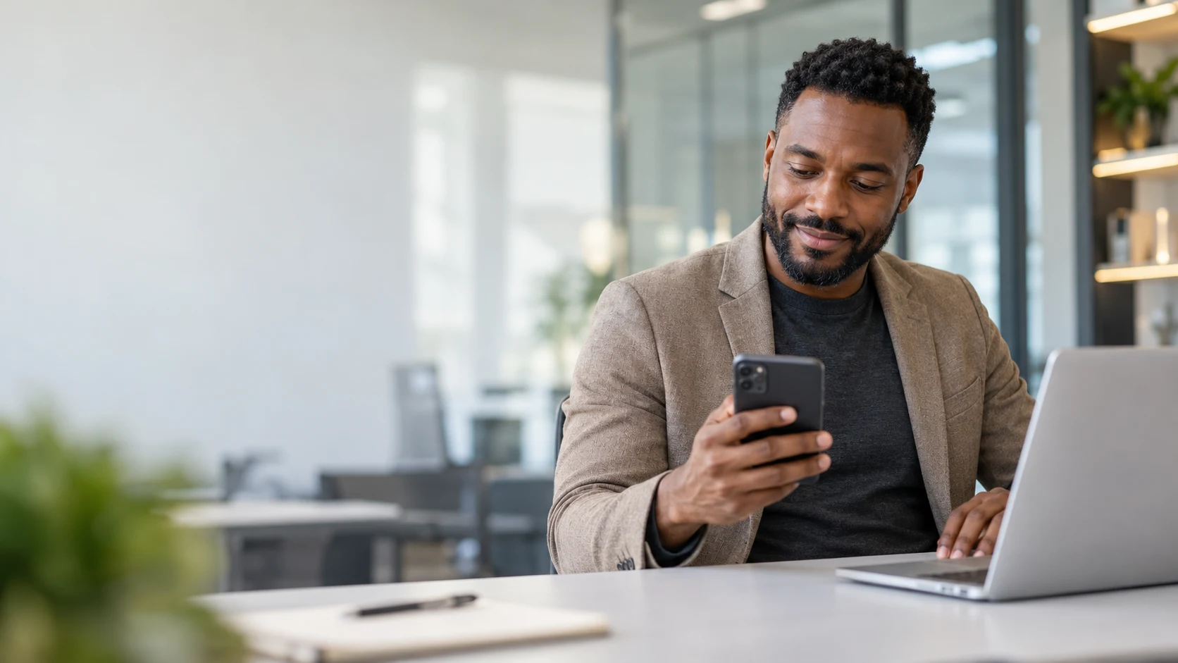 Consultor comercial acompanhando clientes pelo celular ao lado de um notebook.